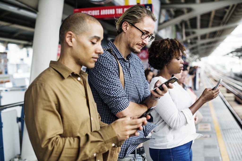 Commuters waiting in a station for a train, and using their mobile devices.