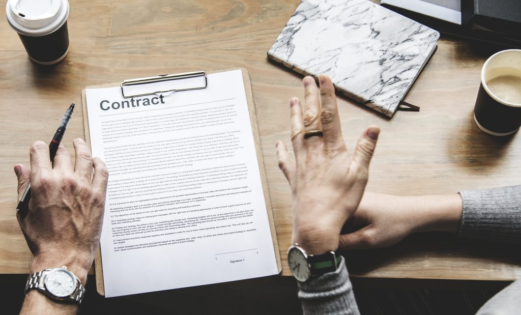 A desk with coffee and paper, with hands preparing to sign a contract