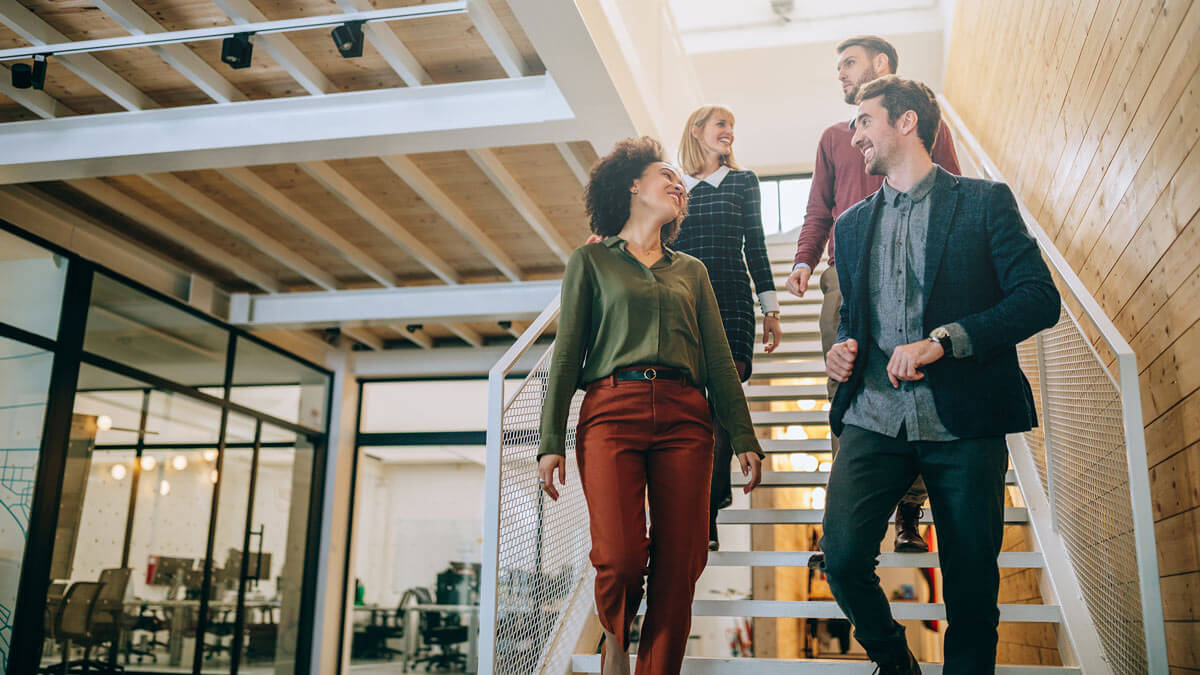 A group of work colleagues walking down some stairs in an office space while smiling and laughing 